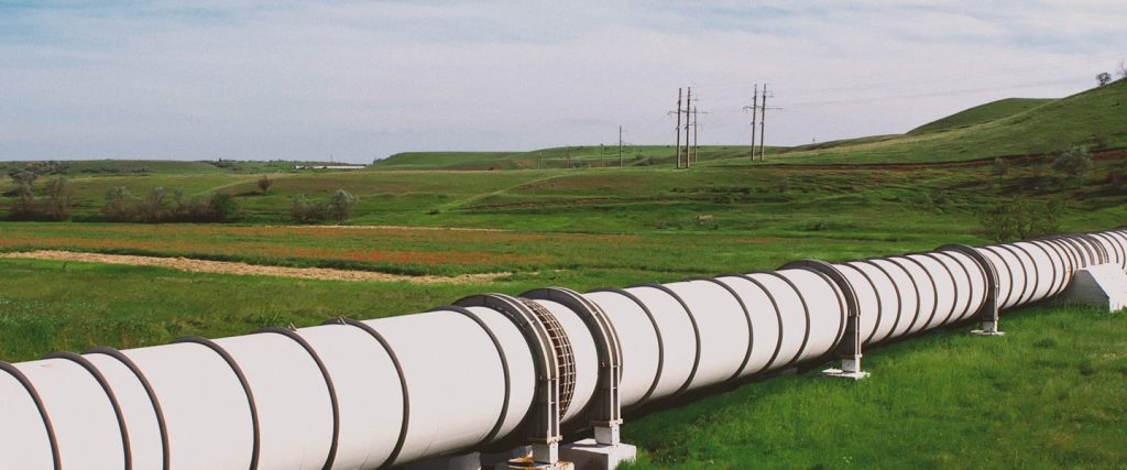 Large carbon pipeline running across open farmland with rolling green hills and utility lines in the background.
