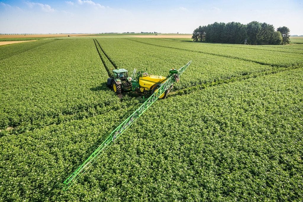 Tractor applying herbicide on a large green crop field with precision boom sprayer during the growing season