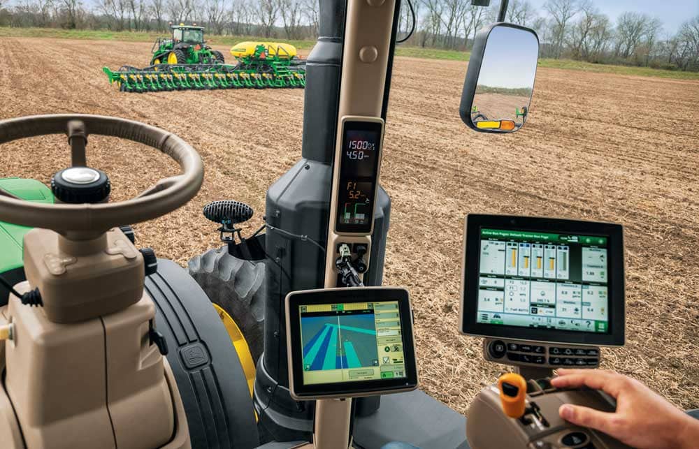 Inside view of a modern tractor equipped with precision agriculture technology, showing GPS-guided controls, digital field maps, and automated planting systems in use on a farm.