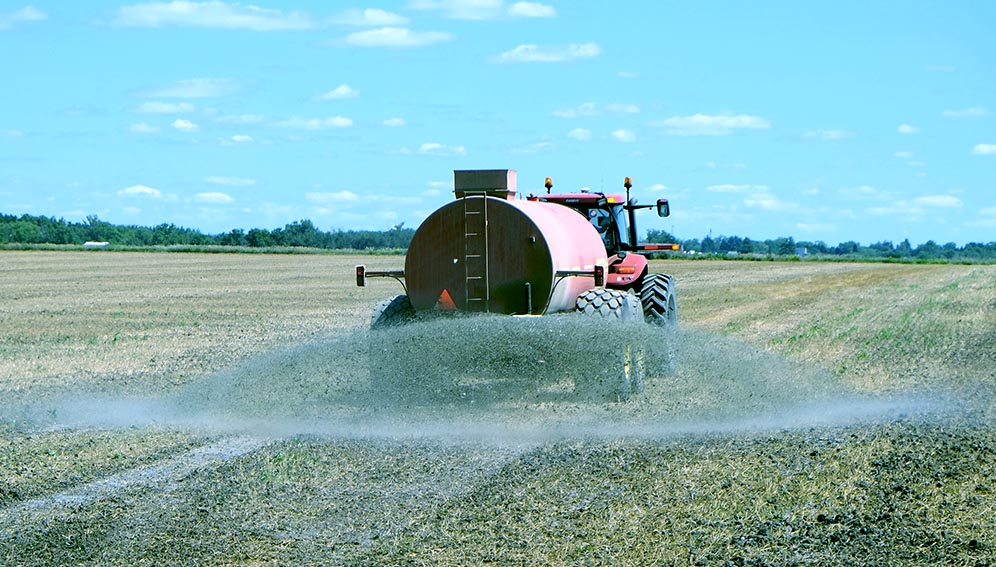 A tractor spreading liquid fertilizer across a harvested field to improve soil nutrients before the next planting season.