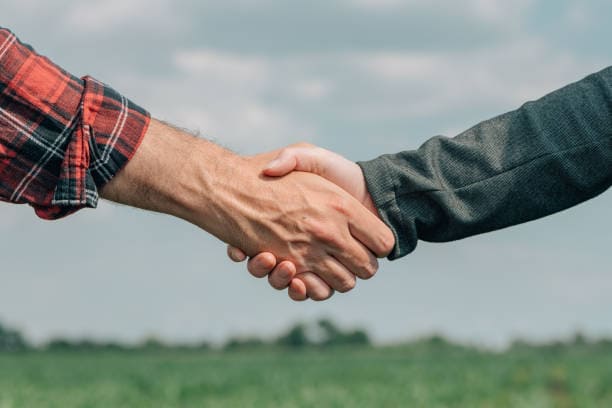 Handshake between two agricultural professionals standing in a farm field, symbolizing networking and partnership in the agriculture industry.
