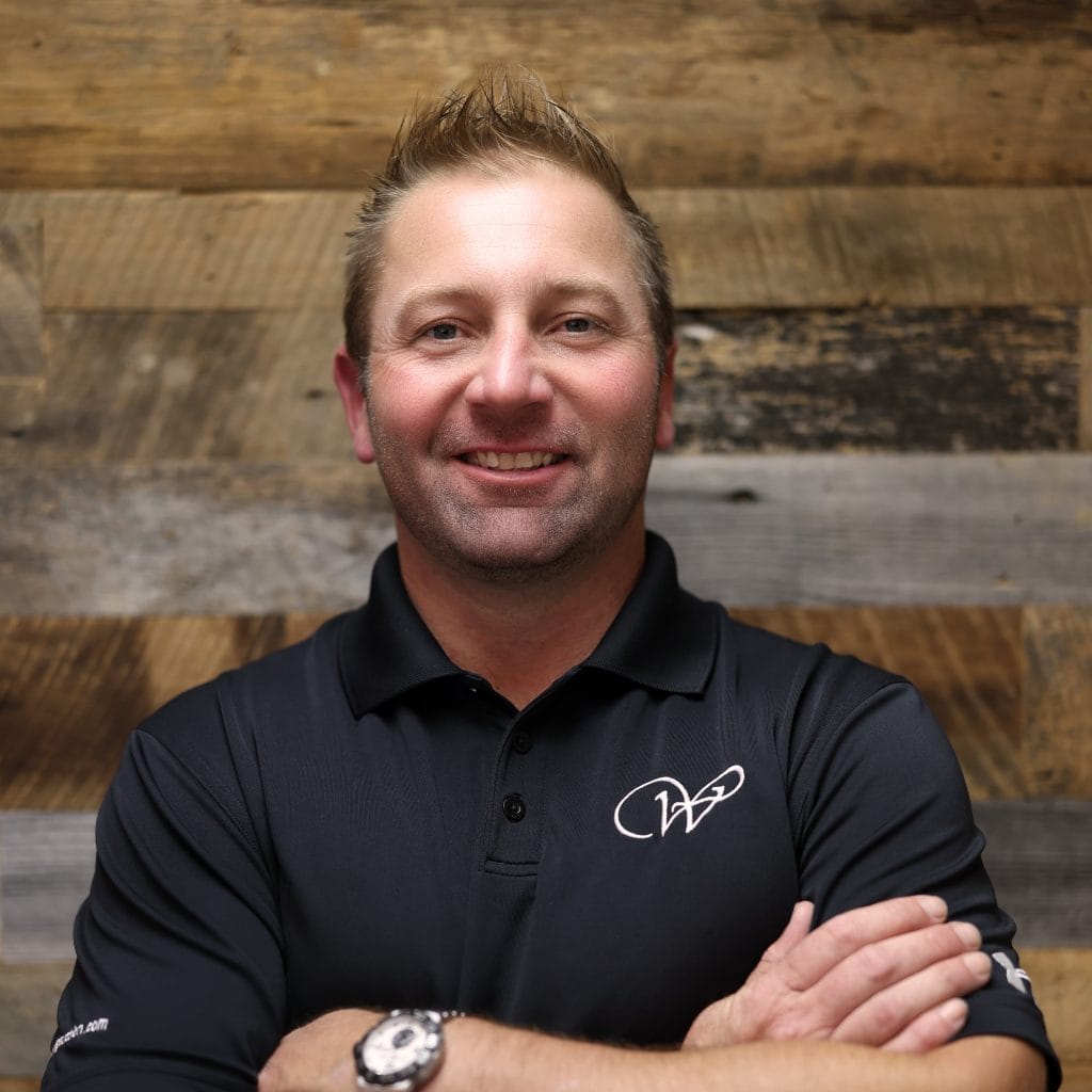 Professional headshot of a Whitaker Marketing Group team member standing with arms crossed against a wood background.