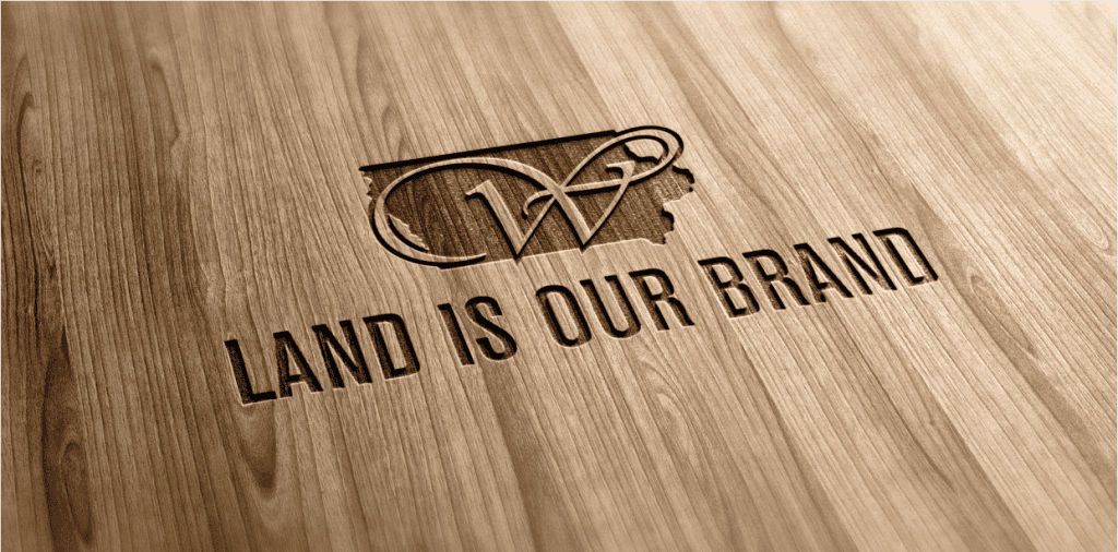 Wood-grain surface featuring the Whitaker Marketing Group logo and the phrase “Land Is Our Brand.”