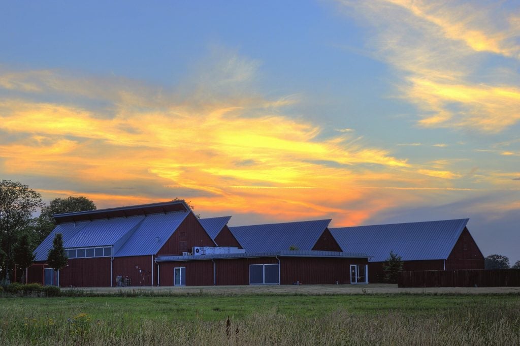 Red agricultural buildings on a rural Iowa farm at sunset with vibrant clouds in the sky.