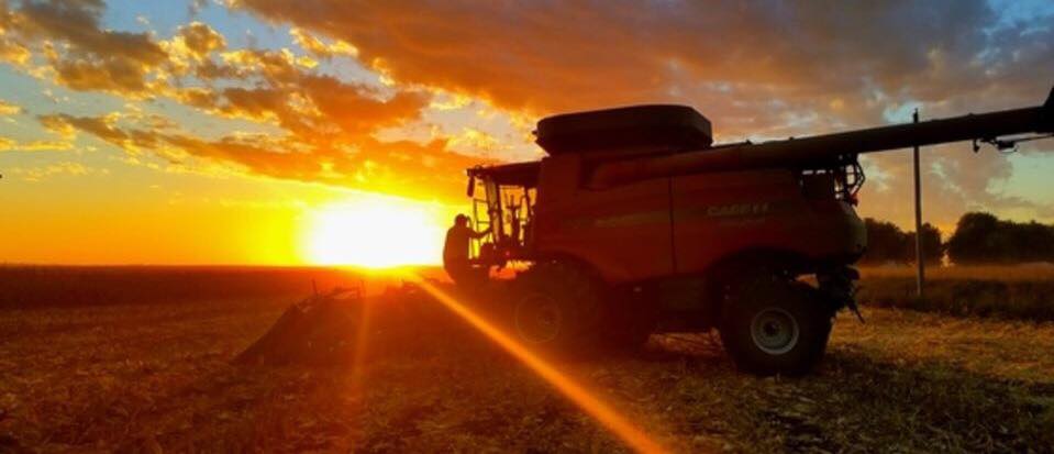 Combine harvesting crops in an Iowa field at sunset highlighting farmland productivity