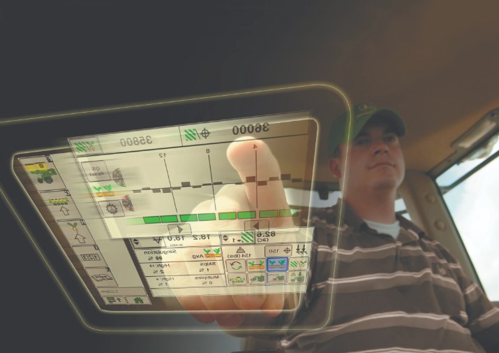 Understanding Farmland Values in Today's Economy A farmer inside a tractor cab using a touchscreen precision agriculture monitor to control field operations.