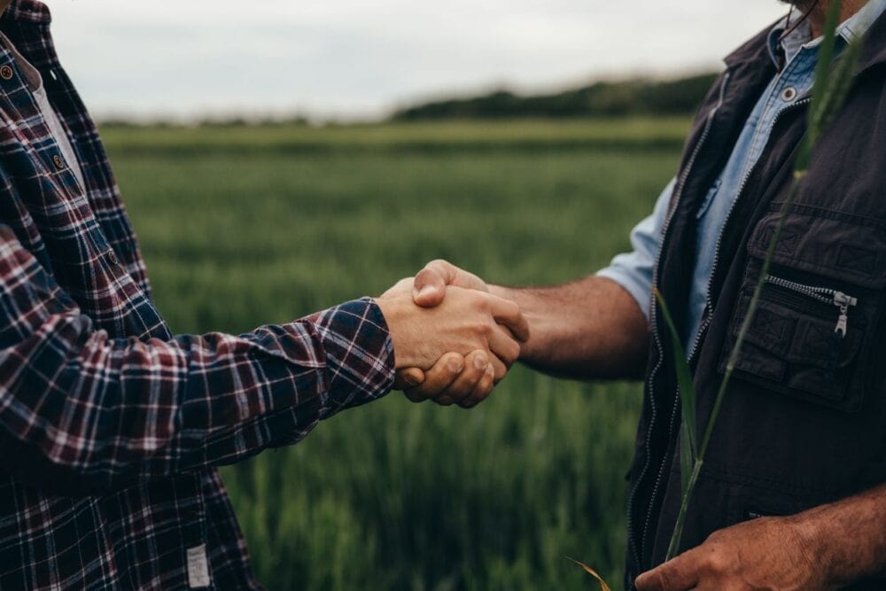 Two farmers shaking hands on an Iowa farmland deal, symbolizing successful agricultural financing and partnership
