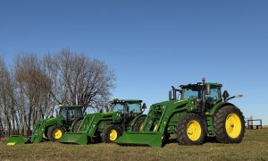 Three John Deere tractors with loaders lined up in a field on a clear day, showcasing equipment ready for auction.