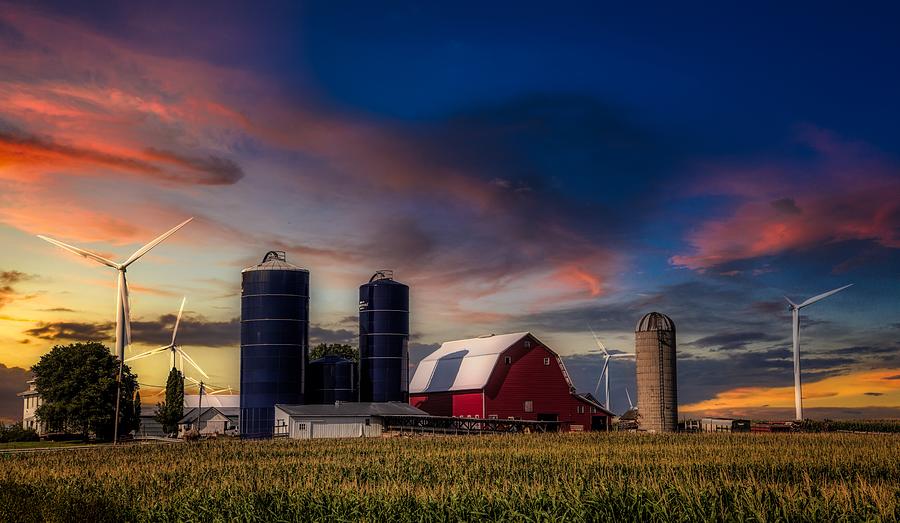 Iowa farmland with red barn, grain silos, and wind turbines at sunset