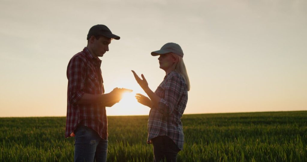 Farmland owners discussing whether to sell agricultural land during sunset in a farm field.