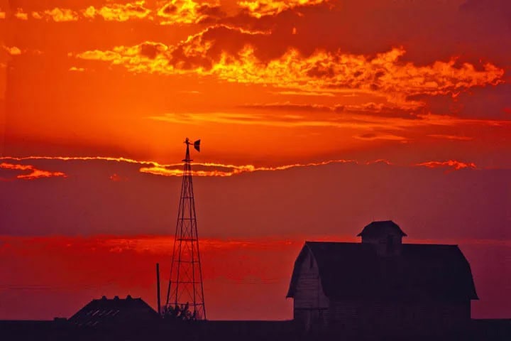 Sunset over Iowa farmland with a barn and windmill representing secure farmland investment.